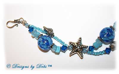 Designs by Debi Jewelry for Charity Piece for August 2010 to raise money for The Donald Paterson Recovery Fund. A one-of-a-kind artisan handmade bracelet with blue ribbon waves round handmade glass beads, thai silver starfish beads, swarovski crystal aquamarine and capri blue bicones, bali sterling silver spacer beads, sterling silver conch shells, tierracast silver scallop shells, light blue cat's eye chips, seed beads and a bali sterling silver hook and eye clasp with extender chain. OOAK one of a kind