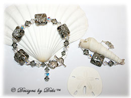 Designs by Debi Handmade Jewelry Aloha Collection Gray Bracelet and Anklet Set. Features gray squareahndmade lampwork beads with floral pattern and cz's, swarovski crystal black diamond and crystal ab bicones, dangle, sterling flower toggle clasp and matching anklet.