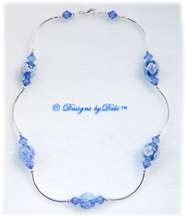 Designs by Debi Handmade Jewelry Aloha Collection Royal Blue Necklace that features blue aloha floral round beads, swarovski crystal sapphire blue bicones, silver curved noodle beads, silver corrugated round beads  and a lobster clasp.